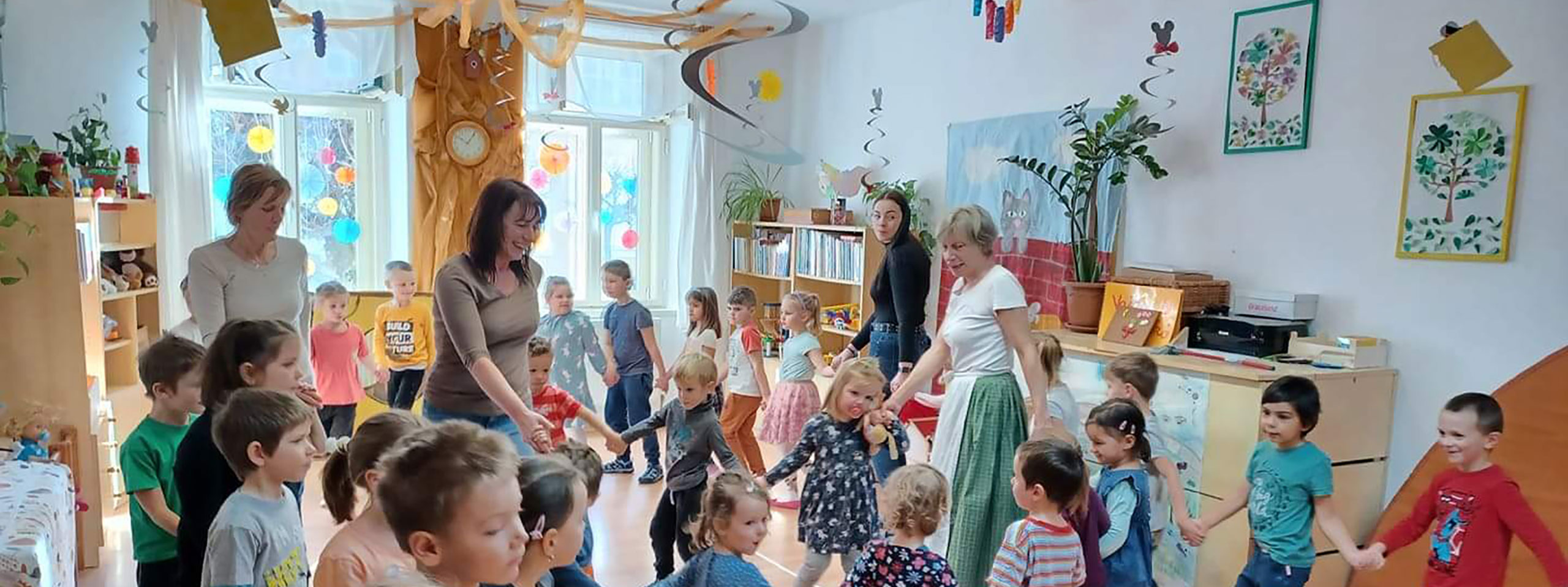 A Fellegvár Óvoda munkatársait ábrázoló fotó, melyen a pedagógusok körben táncolnak a gyerekekkel